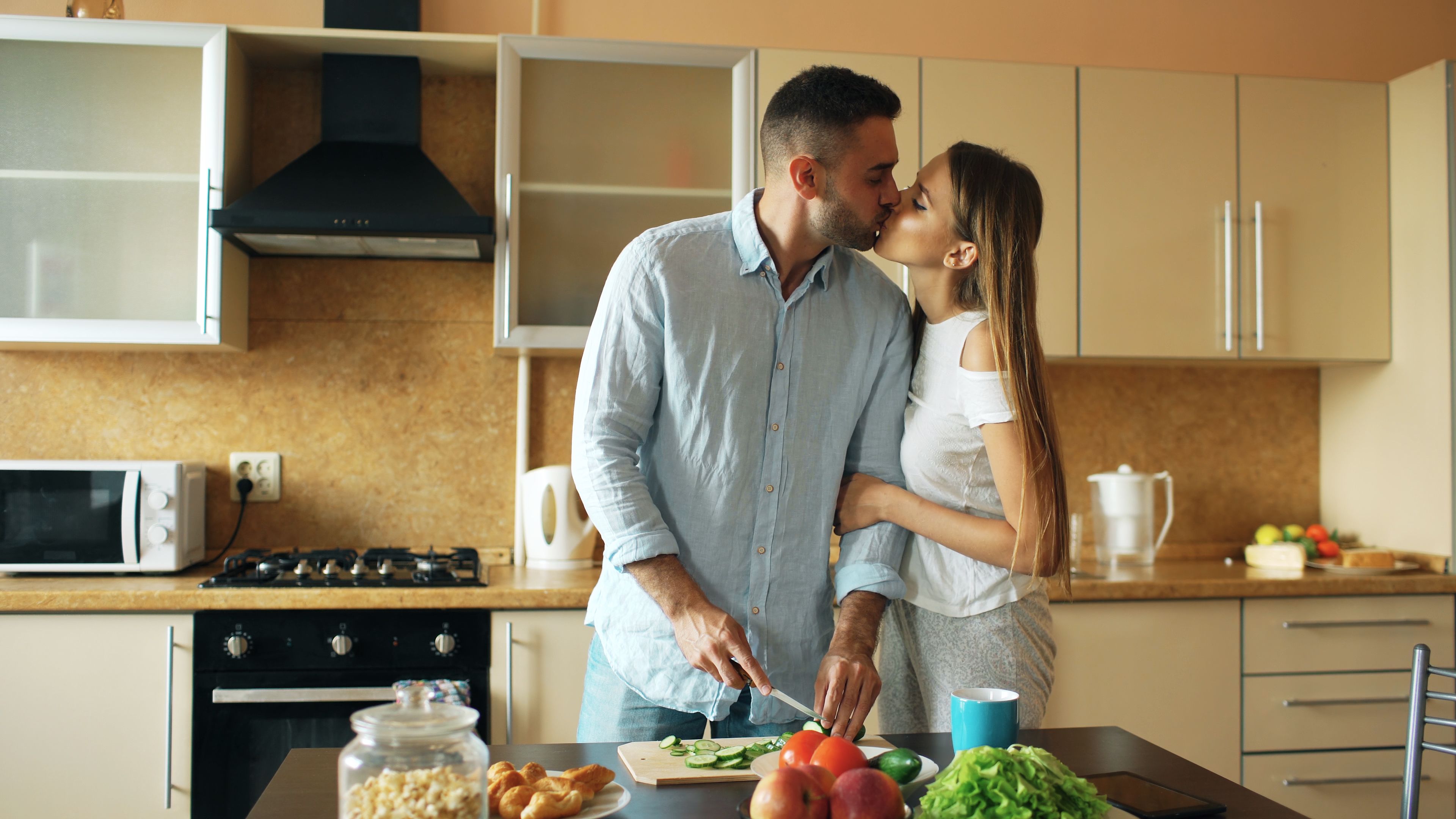 The Zodiac Signs Most Likely to Crave an Authentic ‘Girlfriend Energy’ Connection Couple sharing a kiss while preparing vegetables together in a cozy kitchen.
